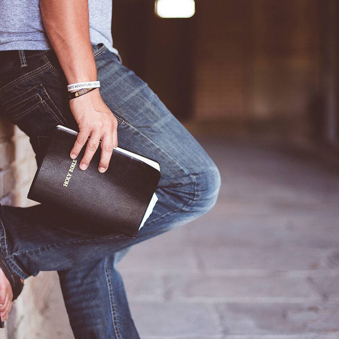 man-holding-Holy-Bible-leaning-on-bricked-wall