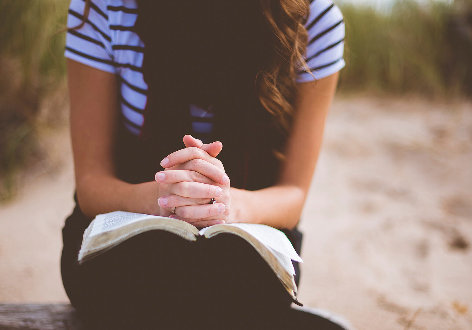 woman-sitting-on-brown-bench-while-reading-book-and-praying